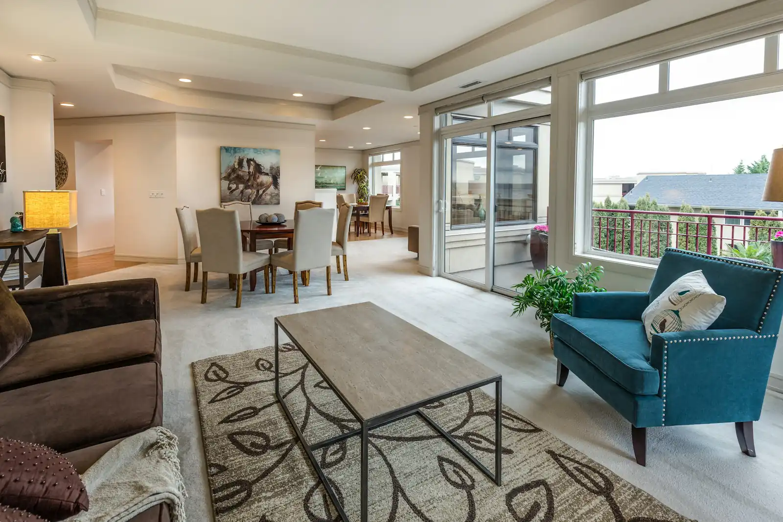 Open condo living and dining room with a teal armchair and a sliding door to the balcony
