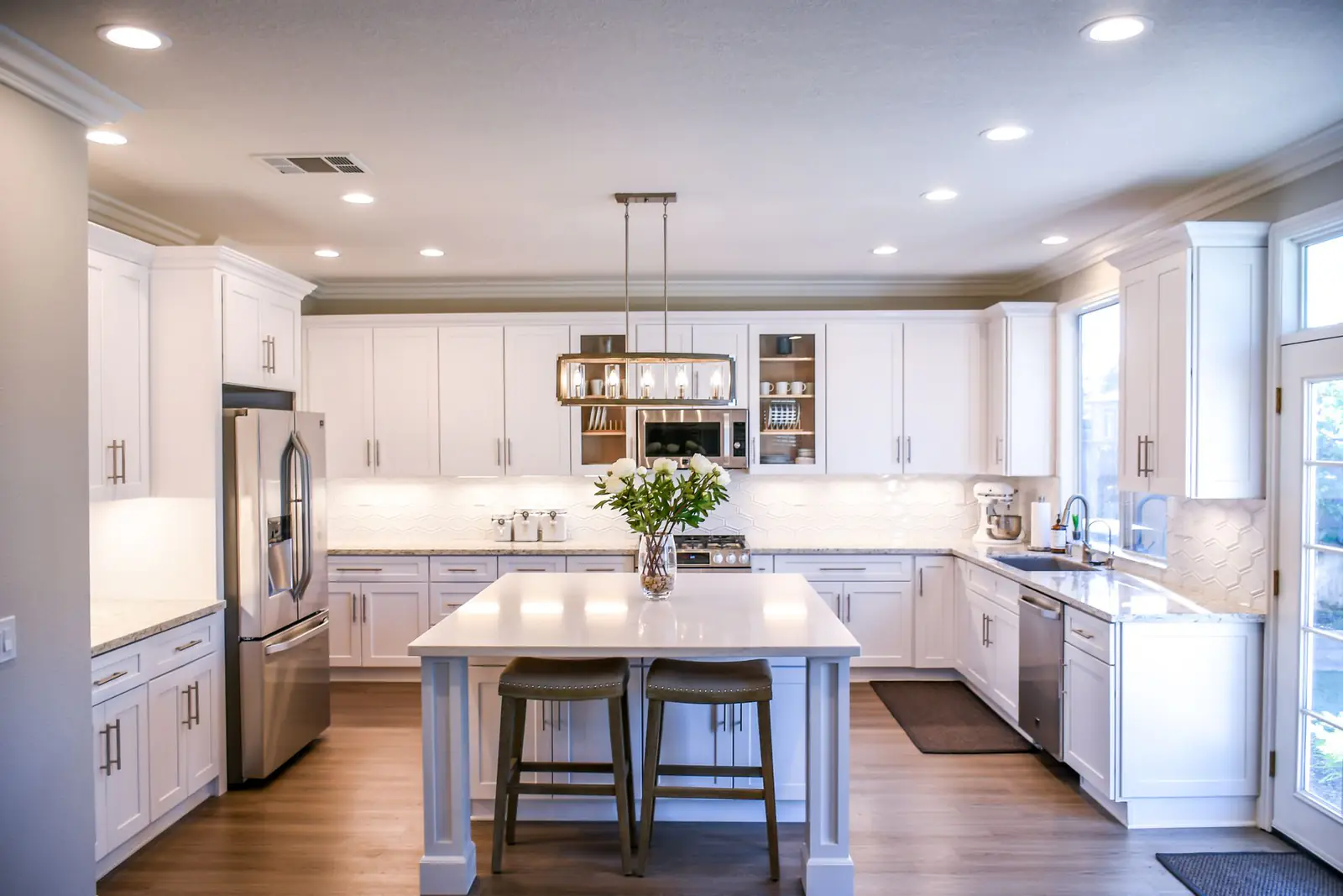 Bright white kitchen with a marble island, pendant lights and wood floors