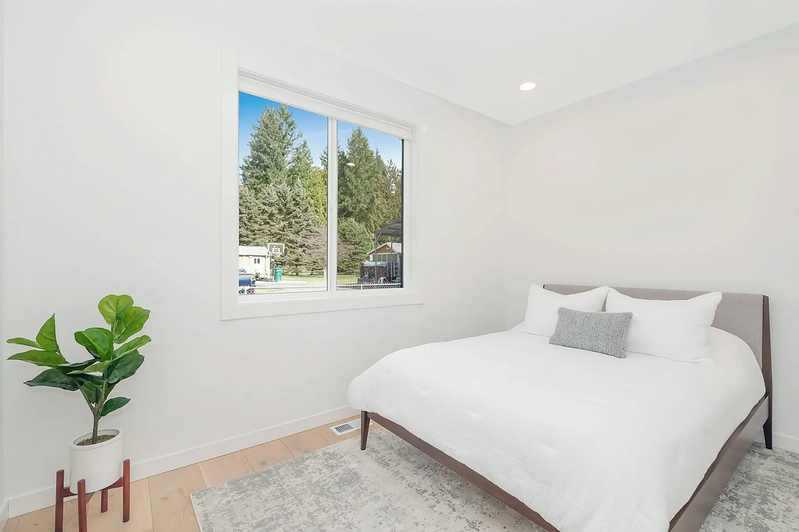 Bright white bedroom with a big window, white bed and new light flooring