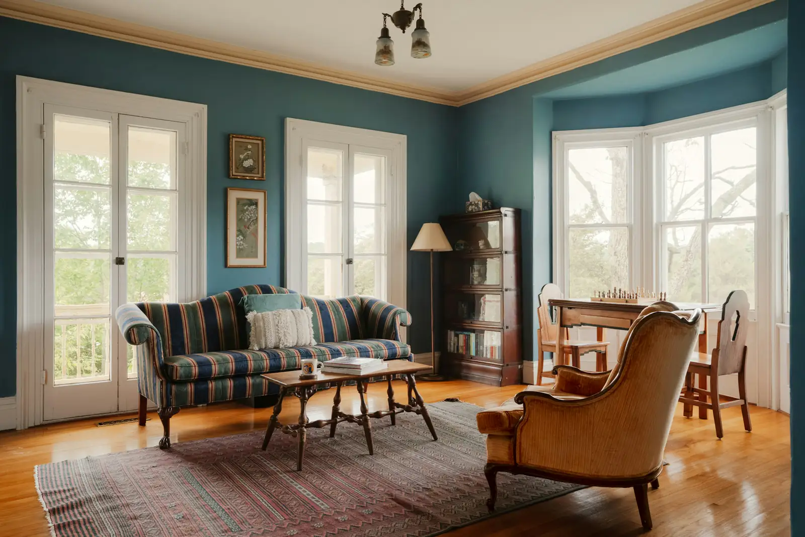 Older living room with teal walls, wood floors, a bay window and original trim